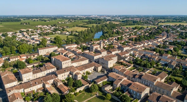 Vue a&eacute;rienne ou perspective urbaine de Saint-Loub&egrave;s en Gironde montrant le tissu urbain avec b&acirc;timents r&eacute;sidentiels et structures architecturales caract&eacute;ristiques de la r&eacute;gion, illustrant le territoire d'intervention de l'entreprise de couverture.