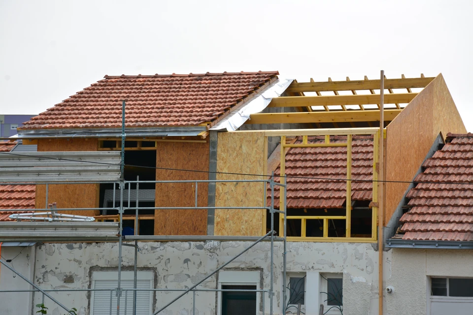 Maison ancienne en pierre ou crépi de style girondain, avec un étage supplémentaire récemment construit en ossature bois clairement visible, montrant la jonction entre l'ancienne structure et la nouvelle surélévation, toiture neuve en tuiles ou ardoises assorties à l'existant, vue de trois-quarts permettant d'appréhender l'ajout d'étage.