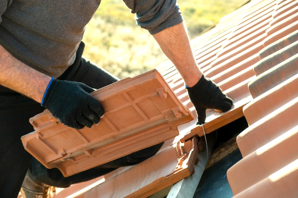 Deux couvreurs professionnels travaillent sur une toiture en chantier au coucher du soleil